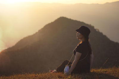 Woman looking away while sitting on mountain during sunset