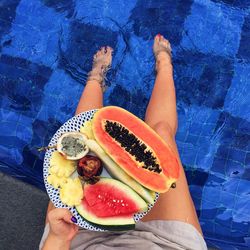 Low section of woman with fruits relaxing at swimming pool
