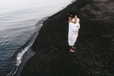 A diverse of lovers a man and a woman embrace under a blanket on the ocean at night outdoor