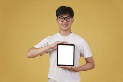 Portrait of smiling young man using smart phone against orange background