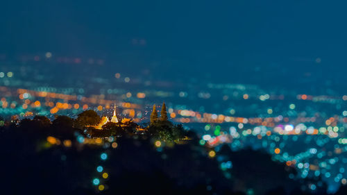 Tilt-shift image of wat phra that doi suthep in illuminated city at night