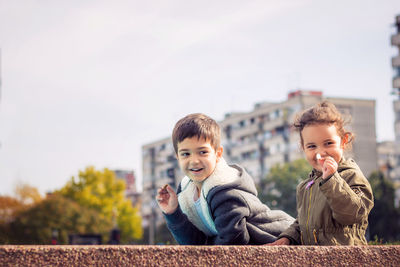 Playful siblings standing against sky in city