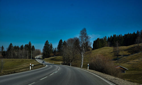 Empty road amidst trees against clear blue sky