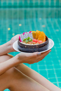 Woman holding smoothie bowl with fresh fruits by swimming pool
