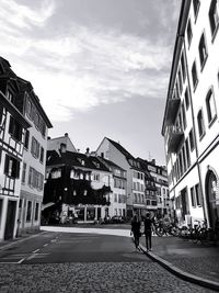 People walking on street amidst buildings in city against sky