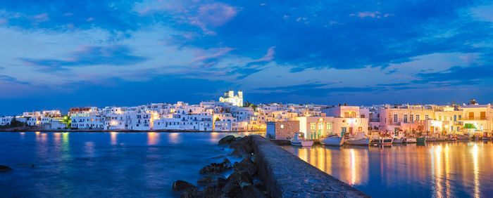 Illuminated buildings by sea against sky at dusk