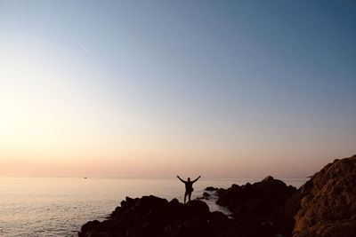 Silhouette person standing on rock in sea against sky