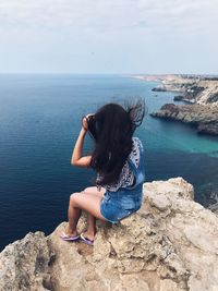 Woman sitting on rock looking at sea against sky