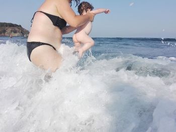 Midsection of woman splashing water in sea against sky