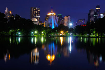 Illuminated buildings by lake against sky in city at night