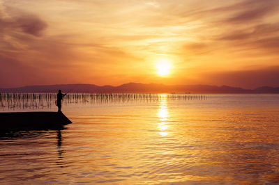 Silhouette man fishing in sea against sky during sunset