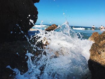 Waves splashing on rocks at shore against clear sky