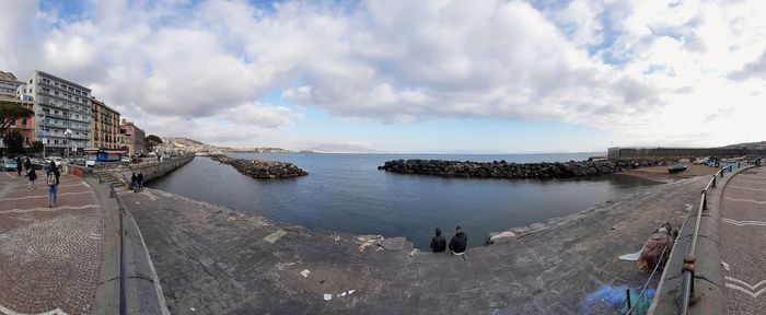 Panoramic view of people on sea by city against sky