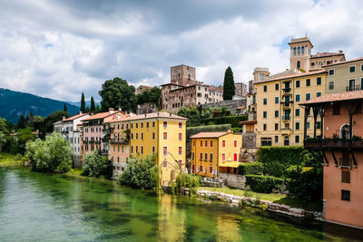 Buildings by river against sky