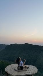 Woman sitting on wood against clear sky