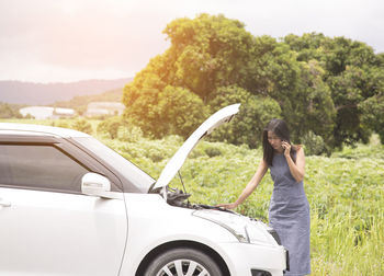Woman standing by car against trees