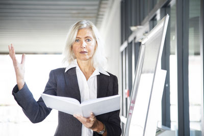 Leader manager older woman standing with book near flipchart