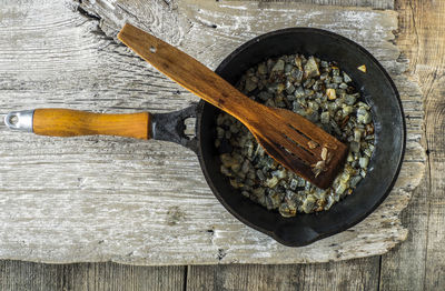 Directly above shot of fried onion in skillet at wooden table