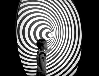 Side view of a boy standing against black background