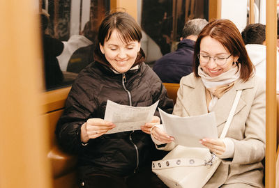 Portrait of two beautiful cheerful girls reading newspapers in a subway car.