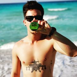 Portrait of young man drinking beer at beach