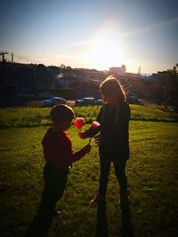 Rear view of children standing on field against sky