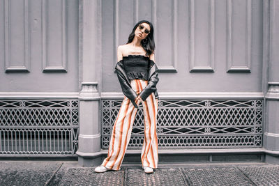 Full length portrait of woman standing against metal structure