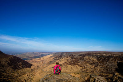 Rear view of woman sitting on rock against landscape