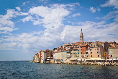 Sea by buildings in city against sky