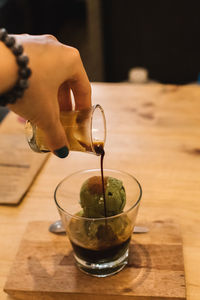 Midsection of person pouring drink in glass on table