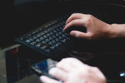 Cropped hand of person using mobile phone and keyboard