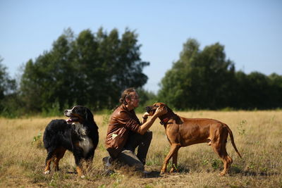 Man playing with dogs on grassy land against sky