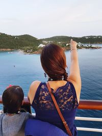 Mother and daughter looking at lake against sky