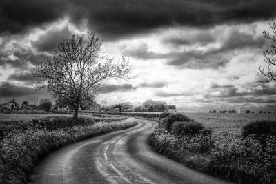 Road passing through field against cloudy sky