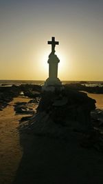 Cross on beach against sky during sunset