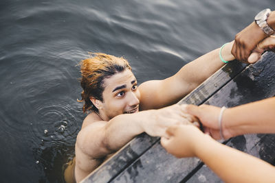 Cropped image of male friends holding hands with young man in lake
