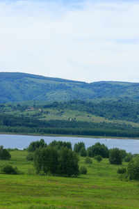 Scenic view of green landscape and river against sky