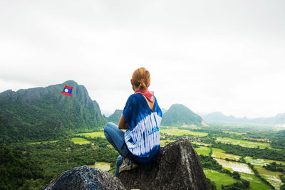 Rear view of woman sitting on rock against sky