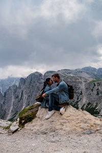 Young man sitting on mountain against sky