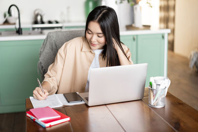 Young woman using digital tablet while sitting on table