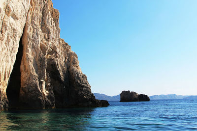 Rock formation by sea against clear blue sky