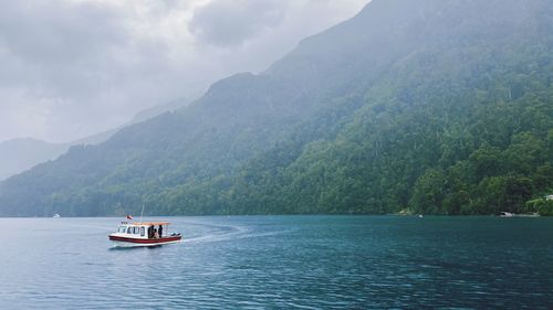 Boat sailing on sea against mountains