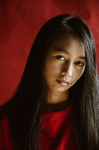 Close-up portrait of young woman standing against red curtain