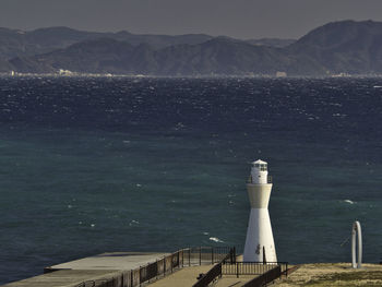 Lighthouse by sea against mountain and sky