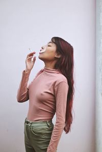 Side view of a young woman drinking against wall