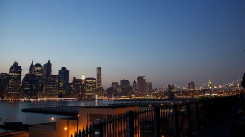 Illuminated buildings by river against clear sky