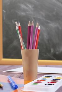 Close-up of multi colored pencils with water color paints on table