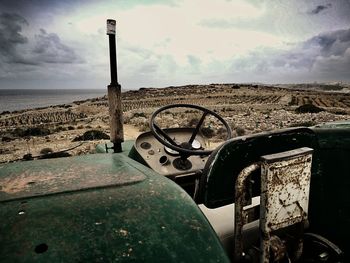 Abandoned car on field by sea against sky
