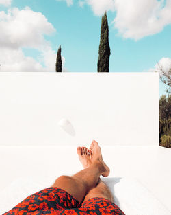 Low section of man relaxing in swimming pool against sky