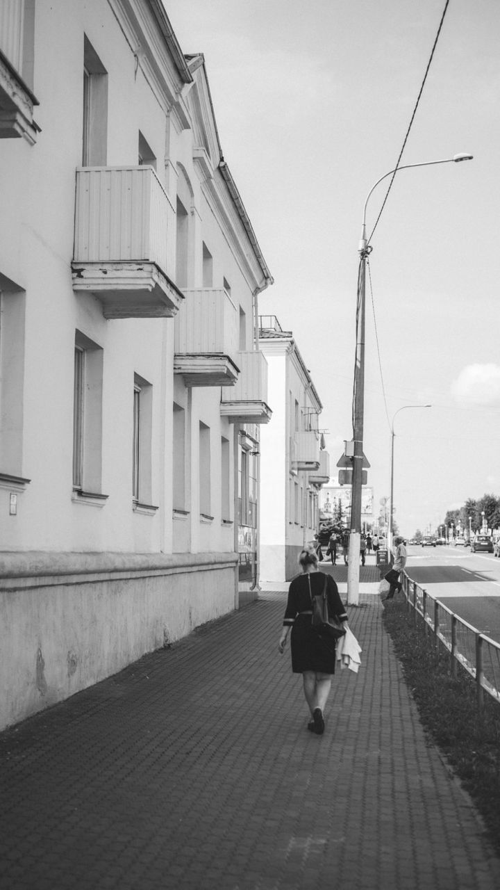 REAR VIEW OF MAN WALKING ON STREET AMIDST BUILDINGS